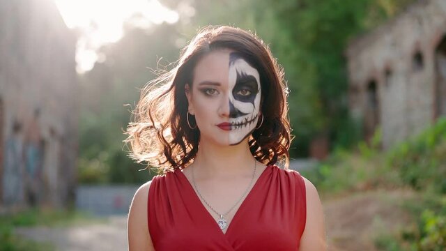 Portrait of a beautiful woman in a red evening dress with makeup on Halloween goes against the backdrop of an abandoned building. A terrible holiday. Slow motion