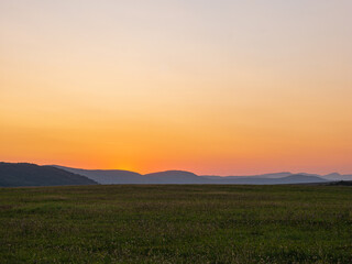 Fototapeta na wymiar Wiese vor Hügellandschaft nach dem Sonnenuntergang