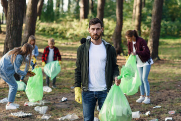 Handsome bearded man with full rubbish pack in background of park where his friends activists...