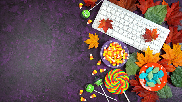 Happy Halloween Trick or Treat theme desktop with candy and lollipops, autumn leaves on stylish purple textured background. Top view blog hero header creative flat lay. Negative copy space.