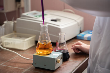 Distant photo of a woman scientist, making a test, dropping something in an erlenmeyer flask, hands...