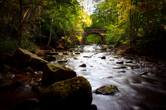 Old brick built bridge over a beck in Yorkshire England the water is flowing over rocks stones and flat boulders. 