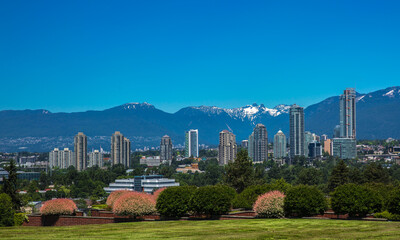 Obraz premium New residential area of high-rise buildings in the city of Burnaby, construction site in the center of the city against the backdrop of snow covered mountain range and blue sky