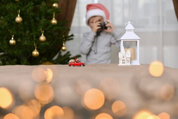 A car with a bag of Christmas gifts goes to the white house of the lantern. A child in a striped cap, with the camera.