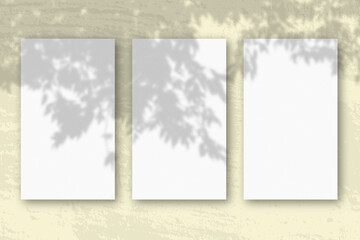 3 vertical sheets of textured white paper on soft yellow table background. Mockup overlay with the plant shadows. Natural light casts shadows from an branch of Apple . Horizontal orientation