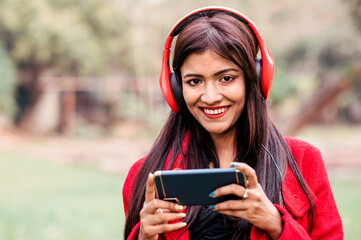Young woman using smartphone and listening music on headphone. Outdoor image with Asian/ Indian model with extra copy space.