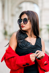 Attractive young woman wearing black sunglasses and red coat. Outdoor shot. Beauty and fashion concept.