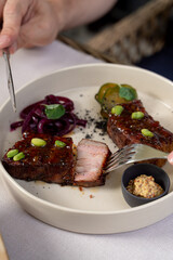 Man is eating beef loin in teriyaki sauce, cutting it with knife and fork, close up on a white tablecloth background