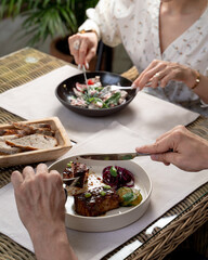 Date of an adult couple in a fancy restaurant, people neatly eating with knife and fork, close up, no faces, hands only visible