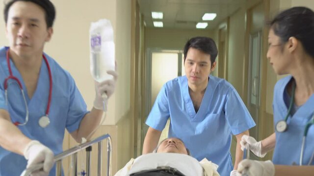 Asian medical team doctor and nurse carrying elder patient unconscious man on gurney or stretcher to emergency room