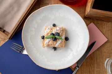 A portion of puff pastry napoleon cake in a wide restaurant dish, top view