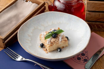 A portion of puff pastry napoleon cake in a wide restaurant dish, top view