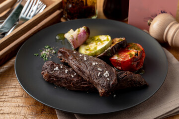 Roasted dry sirloin with grilled vegetables on a black dish in a restaurant, appetizing and fashionable magazine photo