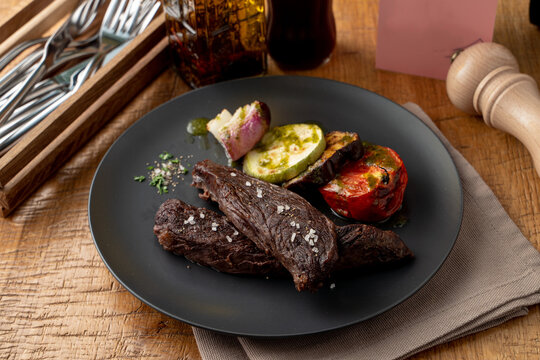 Roasted dry sirloin with grilled vegetables on a black dish in a restaurant, appetizing and fashionable magazine photo