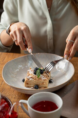 Woman is eating napoleon cake in a restaurant with knife and fork
