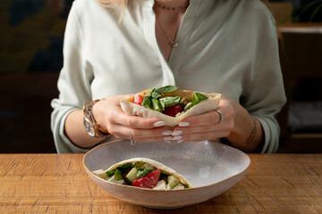 Woman is having lunch with pita, stuffed with salad and feta, wooden table, restaurant photo, no face is visible