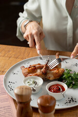 Woman is eating chicken with knife and fork, close up shot, hands only visible