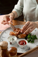 Close up of woman, eating a roasted quail with hands, close up, wooden table in a restaurant