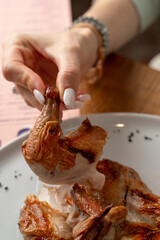 Woman is holding a small roasted quail leg, eating it in a fancy restaurant, wild poultry meal, close up