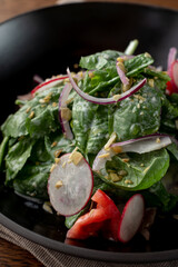 Close up of spinach and duckling salad in a fancy restaurant, served in a black plate, wooden...