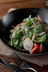 Close up of spinach and duckling salad in a fancy restaurant, served in a black plate, wooden background