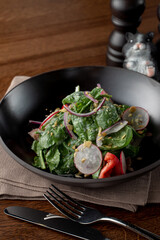 Close up of spinach and duckling salad in a fancy restaurant, served in a black plate, wooden background