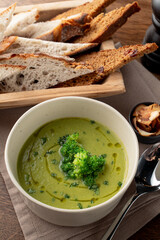 Vertical photo of broccoli cream soup on wooden rustic table with linen cloth on it, top view, brad and spoon aside