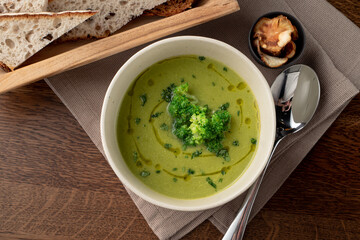 Top view of healthy green broccoli soup on wooden rustic table with linen cloth on it, top view, brad and spoon aside