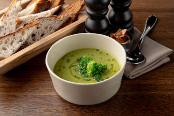 Side view of cream pea soup with bread basket and spoon aside, wooden table, rustic atmosphere commercial photo
