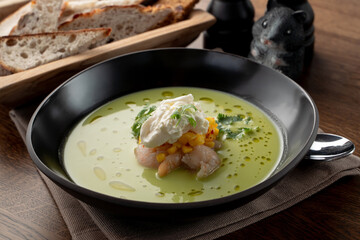 Creamy green soup with crab meat and shrimps on wooden table in a fancy fish restaurant, soft light