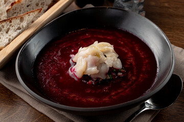 Close up of traditional russian cold soup svekolnik with scallop on wooden table with spoon aside