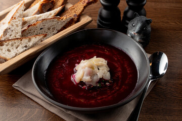 Close up of traditional russian cold soup svekolnik with scallop on wooden table with spoon aside