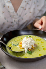 Woman is eating green pea cream soup with seafood with a spoon, close up, hands only visible