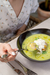 Woman is eating soup with seafood on a summer terrace of a fancy restaurant, close up, hands of a young woman