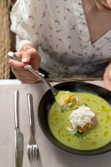 Woman is holding a spoon with green broccoli soup on a summer terrace, outdoor photo, close up