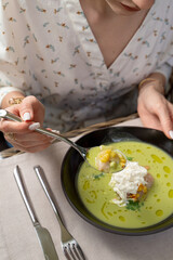 Woman is holding a spoon with green broccoli soup on a summer terrace, outdoor photo, close up