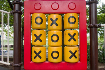 Yellow plastic details with X and O symbols of mechanical Noughts and Crosses game on playground.