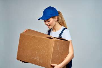A woman in a working uniform with a box in the hands of a delivery service delivery service light background
