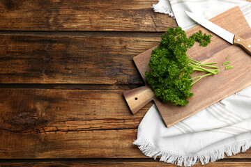 Fresh curly parsley, cutting board and knife on wooden table, flat lay. Space for text