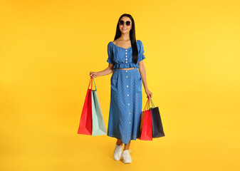 Beautiful young woman with paper shopping bags on yellow background
