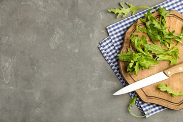 Fresh arugula, cutting board and knife on grey table, flat lay. Space for text