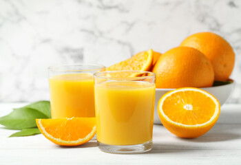 Glasses of orange juice and fresh fruits on white table