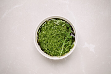 Bowl of tasty arugula pesto on light table, top view