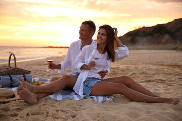 Fototapeta premium Lovely couple having romantic picnic on beach at sunset