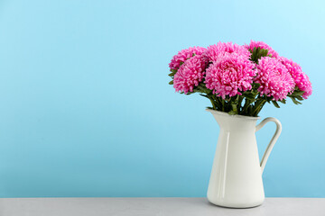 Beautiful asters in jug on table against light blue background, space for text. Autumn flowers
