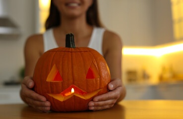 Woman holding pumpkin jack o'lantern at wooden table indoors, closeup with space for text....