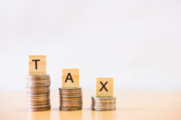 Selective focus at wood tax sign on top of decrease stack of money on the white copy space background. Business or personal tax payment, expense that need to manage and plan.