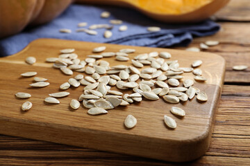 Raw pumpkin seeds on wooden board, closeup
