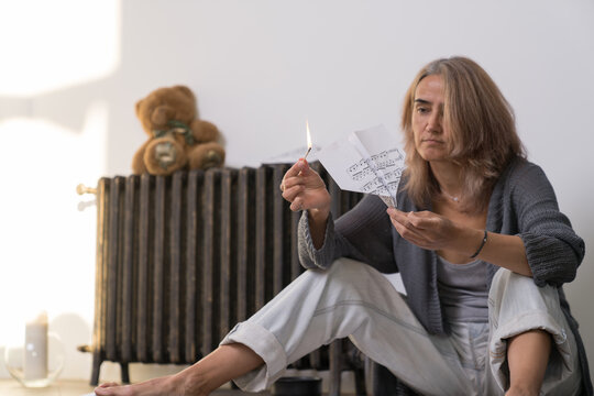 a woman sitting on the floor sets fire to an airplane made of paper sheets on which notes are written