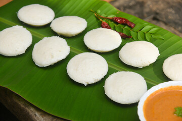 Indian idly served on traditional banana leaf vegetarian food. Lots of many fresh steamed Indian Idly , Idli rice cake. South Indian breakfast idly sambar or Sambhar red coconut chutney